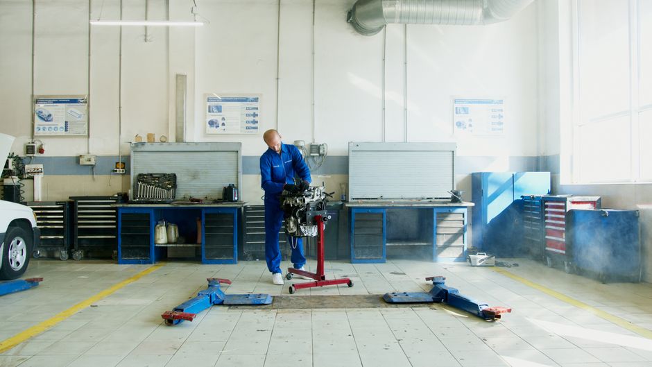 Mechanic inspecting car engine in well-equipped auto repair shop.